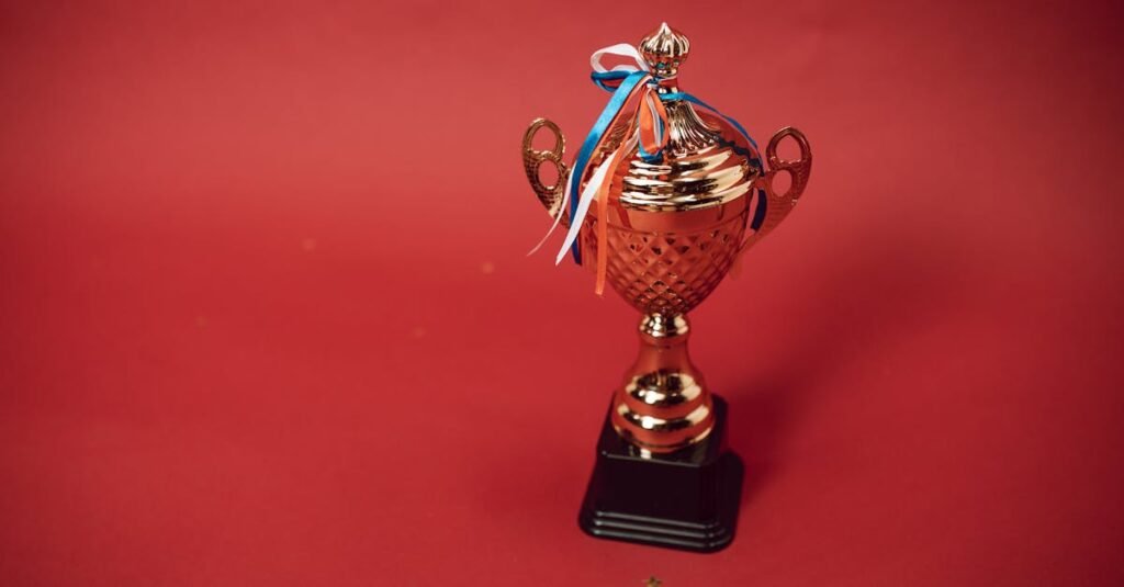 pexels-photo-7005687-7005687 Golden trophy cup with red, blue, and white ribbons on a red backdrop symbolizes achievement and success.